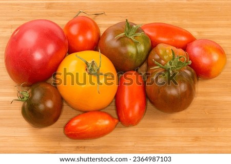 Freshly harvested ripe whole varicolored tomatoes of different varieties on the wooden cutting board
