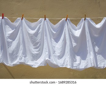 Freshly Laundered White Linen Hanging Outdoors  On A Washing Line In Front Of A Yellow Ochre Wall In The Sunshine 