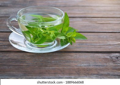 Freshly made hot aromatic mint tea in a glass cup and fresh leaves on a wooden table close-up. Concept of a healthy lifestyle.