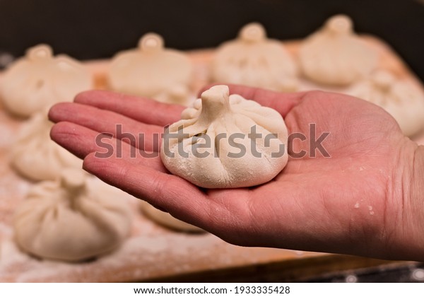 Freshly made khinkali in a woman\'s hand against a\
background of blurry\
same