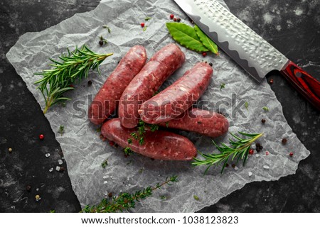Freshly made raw breed butchers sausages in skins with herbs on crumpled paper.