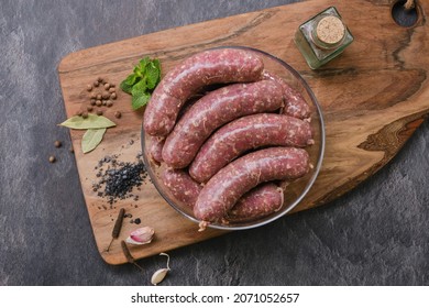 Freshly made raw sausages mix in skins with herbs in a glass bowl. Raw homemade bratwurst sausages with spices, garlic, grate, mint from a meat grinder and wooden kitchen board. Focus on wurst