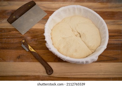 Freshly made sourdough bread in a proofing basket on a wood work surface with a lame and bench knife - Powered by Shutterstock