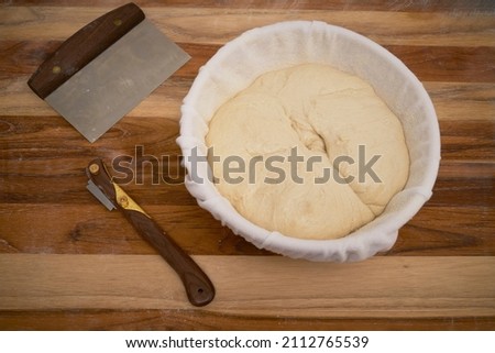 Freshly made sourdough bread in a proofing basket on a wood work surface with a lame and bench knife Imagine de stoc © 
