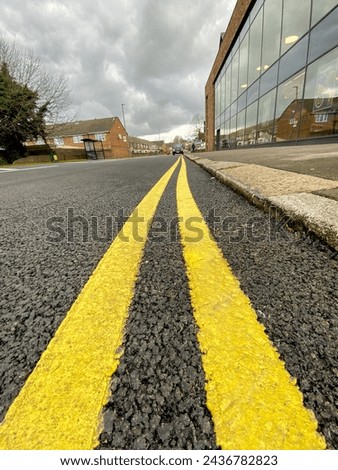 Freshly painted two yellow line or double yellow lines on a newly made road, warning vehicle users that parking is not permitted at anytime.  No parking warning anytime on this section of UK road.