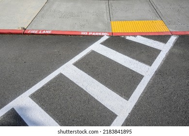 Freshly Painted White Crosswalk Marking Leading To A Yellow Painted ADA Sidewalk Access In A Fire Lane
