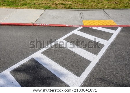 Freshly painted white crosswalk marking leading to a yellow painted ADA sidewalk access in a fire lane
