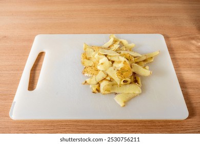 Freshly peeled potato skins scattered on a non-wooden cutting board, showcasing the rustic beauty of kitchen prep work. - Powered by Shutterstock