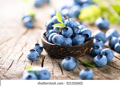 Freshly picked blueberries in wooden bowl. Juicy and fresh blueberries with green leaves on rustic table. Bilberry on wooden Background. Blueberry antioxidant. Concept for healthy eating and nutrition