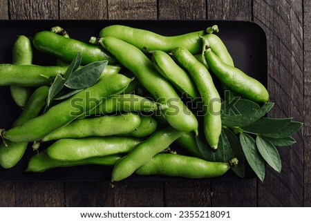 Freshly picked green fava beans on a wooden table.