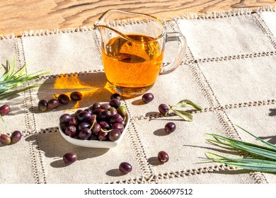 Freshly picked olive tree fruits and olive oil in glass saucepan. First cold pressed oil. Olea europaea. Napkin made of unpainted linen in rustic style - Shutterstock ID 2066097512