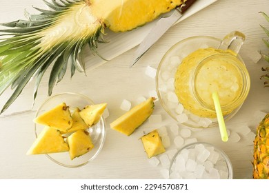 Freshly prepared pineapple soft drink with a lot of ice on a wooden kitchen bench with fruit and a bowl with ice around it. Top view. Horizontal composition.