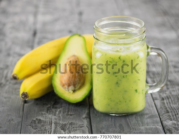 A freshly prepared smoothie of avocado, banana,\
orange, lemon, parsley and kiwi on a wooden table. Diet vegetarian\
food.