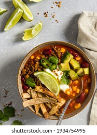 Freshly prepared vegan spicy mexican soup with beans and sweetcorn, garnished with fried tortilla chips, vegan sour cream, piece of lime, avocado and coriander.  - Shutterstock ID 1934754995