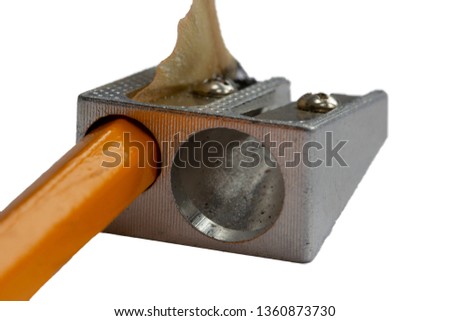Freshly sharpened pencil and pencil sharpener on white background. Yellow pencil in a manual steel sharpner with wood swirl. Against white background. Pencil sharpner at work.