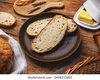 Freshly sliced piece of artisan bread with butter on a wooden table, surrounded by rustic kitchen items - Powered by Shutterstock