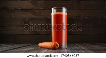 Freshly squeezed carrot juice in a high glass on wooden background. Roustic scene, fresh fruit drink