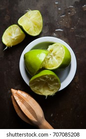 Freshly squeezed limes in white ramekin against dark tin background with wooden juicer