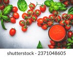 Freshly squeezed tomato juice in a glass and red cherry tomatoes on branches with green basil on gray table, food background, top view