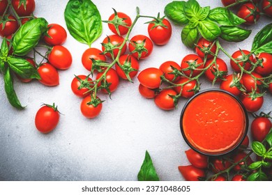 Freshly squeezed tomato juice in a glass and red cherry tomatoes on branches with green basil on gray table, food background, top view