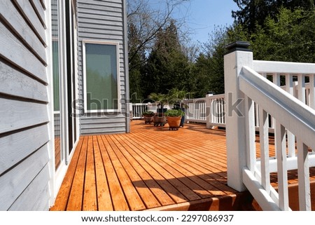 Freshly stained walk out home outdoor cedar wood deck with potted plants in bloom 