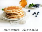 Freshly tasty stack of pancakes on the plate, maple syrup and blueberries isolated on a white background. Delicious homemade breakfast or lunch. Directly above.