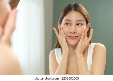 Freshness, nice healthy. Beautiful asian young woman, girl looking on reflection in mirror, hand touching face with makeup cosmetic, skin care routine at home. Happy smile female with natural beauty.