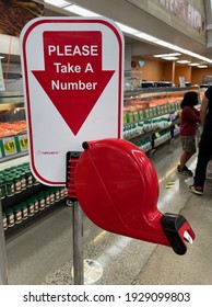 FRESNO, UNITED STATES - Feb 22, 2021: A Photo Of A Red Tall Standing Sign That Reads: Please Take A Number With Arrow Dispenser For Shoppers