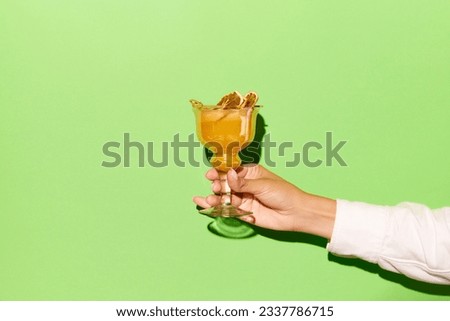 Friday mood. Female hand holding glass with orange juice cocktail with vodka on light green background. Concept of alcohol, drinks, party, ad.