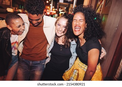 Friday Night Fun. Group Of Vibrant Young People Laughing Joyfully While Walking Together In The City At Night. Four Multicultural Friends Going Out Together On The Weekend.