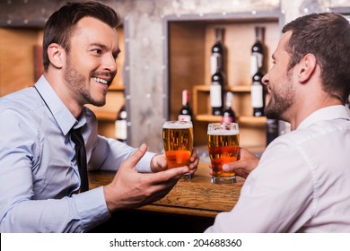 Friday Night Fun. Two Cheerful Young Men In Shirt And Tie Talking To Each Other And Gesturing While Drinking Beer At The Bar Counter 