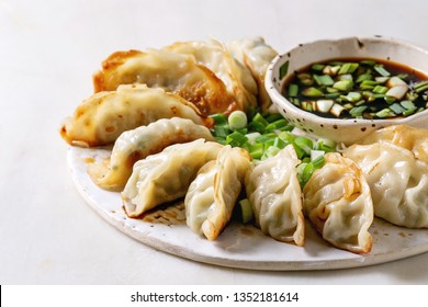 Fried asian dumplings Gyozas potstickers in white ceramic plate served with bowl of soy onion sauce over white marble table. Close up. Asian dinner
