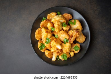 Fried in batter Cauliflower florets served on a black plate on a grey concrete table with ingredients, view from above, close-up, flatlay, copy space (Turkish name; karnabahar kizartmasi)