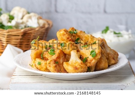 Fried in batter Cauliflower florets served on a black plate on a grey concrete table with ingredients, view from above, close-up, flatlay, copy space (Turkish name; karnabahar kizartmasi)