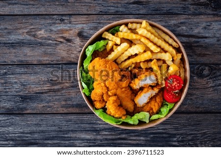 Fried breaded chicken nuggets served with French fries and vegetables on wooden table 