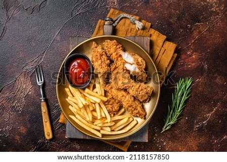 Fried Breaded chicken tender strips with french fries and tomato ketchup on a plate. Dark backgrund. Top view