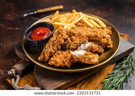 Fried Breaded chicken tender strips with french fries and tomato ketchup on a plate. Dark backgrund. Top view.