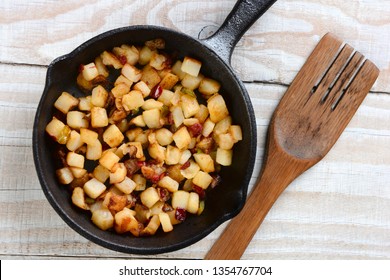 Fried Breakfast Potatoes in a cast iron skillet. Peppers, onions and potato cubes fill the skillet resting on a rustic farmhouse style kitchen table with a wooden fork.