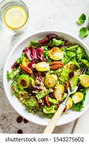 Fried brussels sprouts salad with quinoa, cranberries and nuts in a white bowl. Healthy vegan food concept.