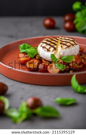 Fried Camembert cheese with cherry tomatoes, capers and basil. Baked Camembert or brie cheese with tomatoes on black background. Gourmet traditional Breakfast. Selective focus.