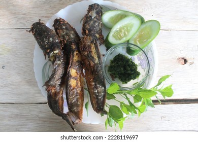 Fried catfish, sambal and fresh vegetables in a white plate on a wooden table - Shutterstock ID 2228119697