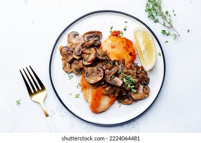 Fried chicken breast fillet with champignon mushrooms and onion in white wine sauce with thyme on plate, white table background, top view - Shutterstock ID 2224064481
