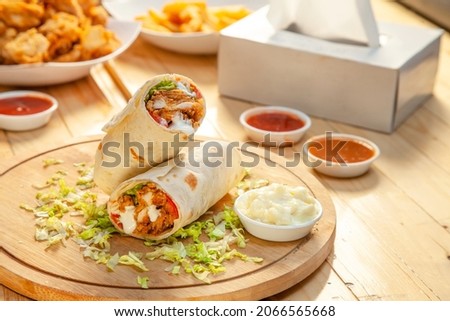 Fried chicken crispy tortilla roll with lettuce garnishing served with dips and sauces on a round wooden plank.