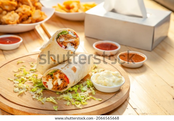 Fried chicken\
crispy tortilla roll with lettuce garnishing served with dips and\
sauces on a round wooden\
plank.