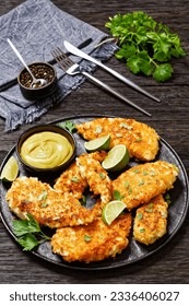 fried chicken cutlets under breadcrumbs and parmesan cheese crust on black plate with mustard and lime on dark wooden table, close-up, vertical view