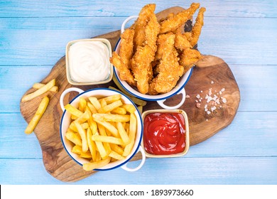 Fried chicken dippers in bucket with sauce on blue background.Chicken breaded strips in small ceramic pots with ketchup and white sauce and french fries. - Powered by Shutterstock