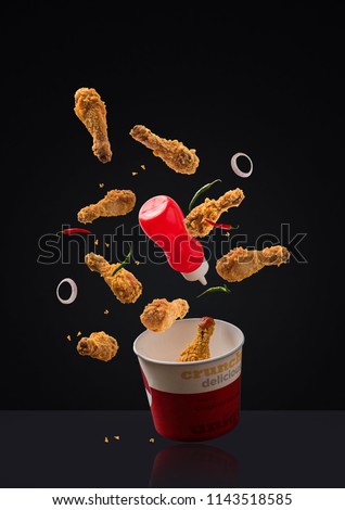 fried chicken legs flying with ketchup bottle, green and red chilli, onion rings and paper container over plain background
 Stock photo © 