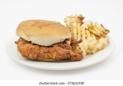 Fried Chicken Sandwich On Plain Bun With Waffle Fries Served On A White Paper Plate.