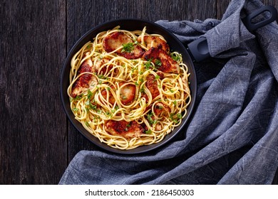 Fried Chicken Scampi Pasta In Frying Pan On Dark Wooden Table With Kitchen Towel, Horizontal View From Above, Flat Lay, Free Space