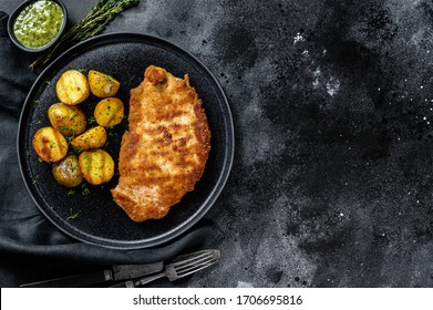 Fried Chicken schnitzel with baked potatoes. Black background. Top view. Copy space